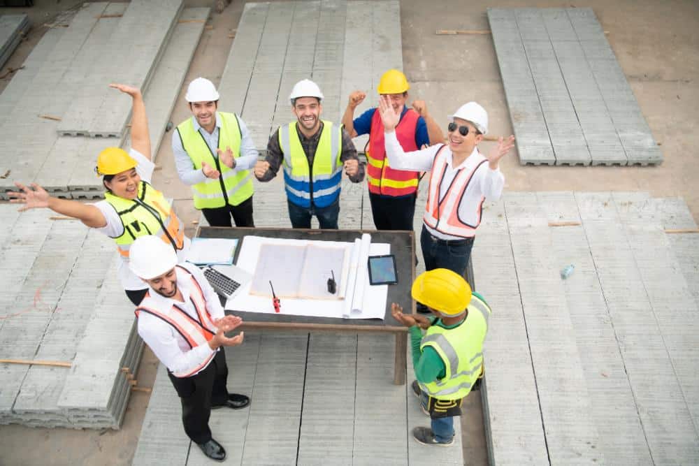 Construction team celebrating success at a building site with safety gear and plans.