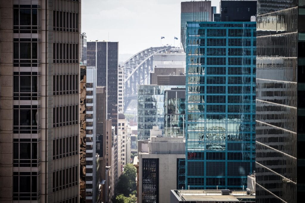 Skyscrapers in downtown city with modern glass and steel buildings, cityscape, and Sydney Harbour Bridge.